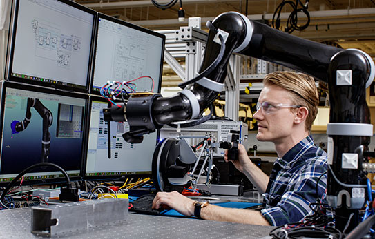 a person looking at four monitors with a robotic arm nearby