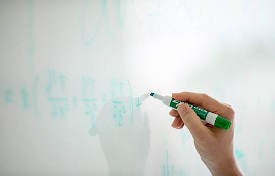 A hand holding a green marker and writing on a whiteboard