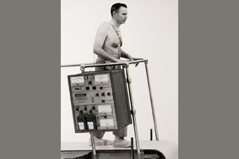 Person using an early version of the treadmill; the handlebars are two basic poles attached to a very large machine