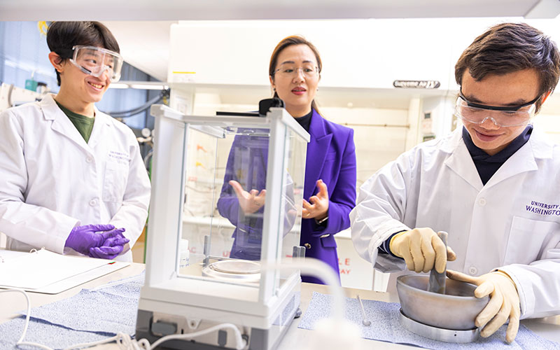 Jie explaining to students wearing lab coats and protective gear as they work with lab instruments