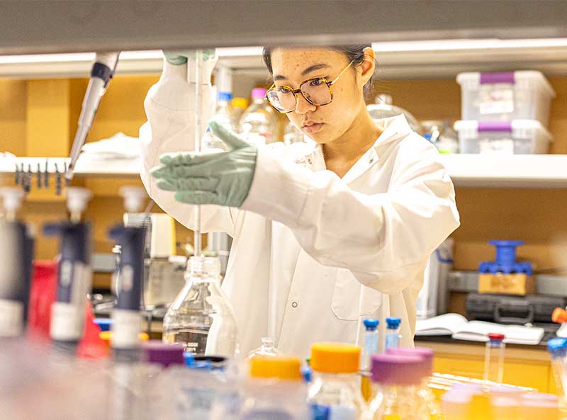 Student wearing gloves and lab coat performing tests in lab