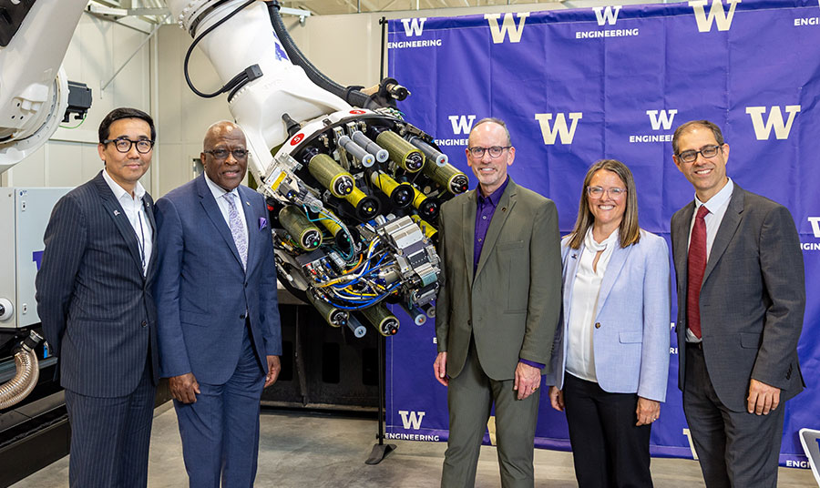 Group photo taken during UW event. Group is in front of large, advanced machinery.