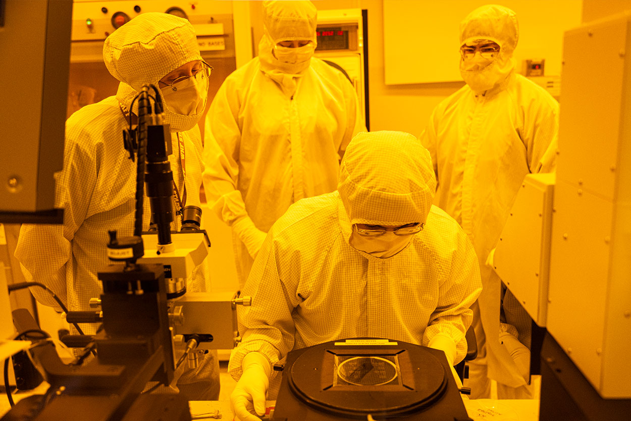 Researchers wearing full protective gear in a lab under yellow lighting