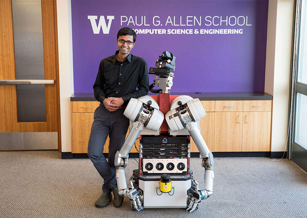 Siddhartha smiling while leaning on robot
