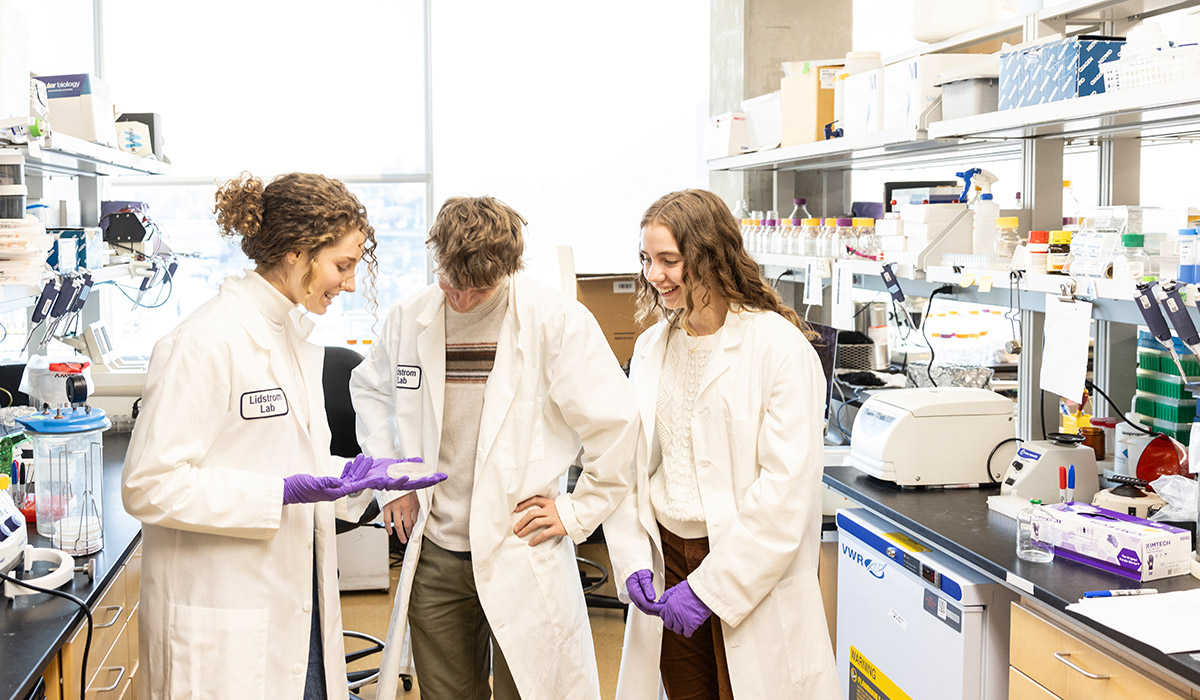 Students wearing lab coats gather around agar plate