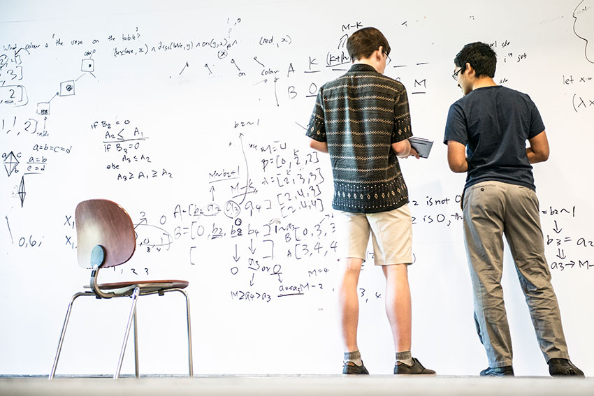 Two students standing in front of a white board