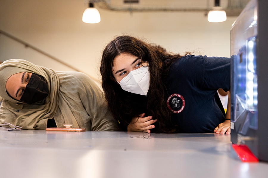 Two students looking sideway at an engineering device