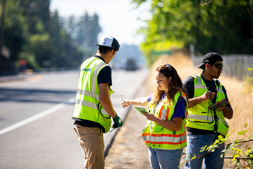 Three students taking measurements at the side of a road