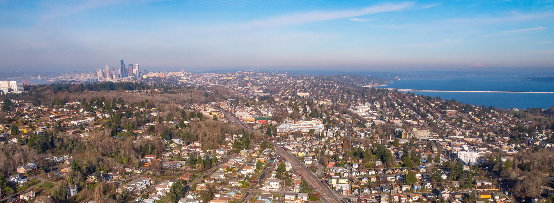 An aerial shot of Seattle showing a large road surrounded by neighborhoods and businesses. There is water on the right and downtown is in the top left.