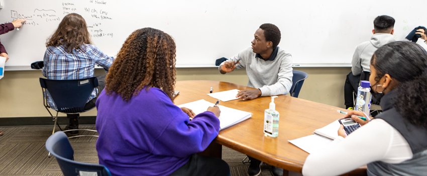Students studying at a table looking at white board