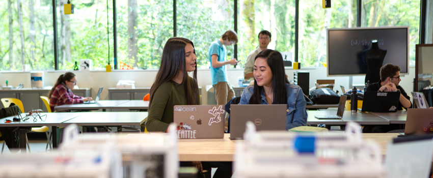 Two students studying at a library sitting with their laptops