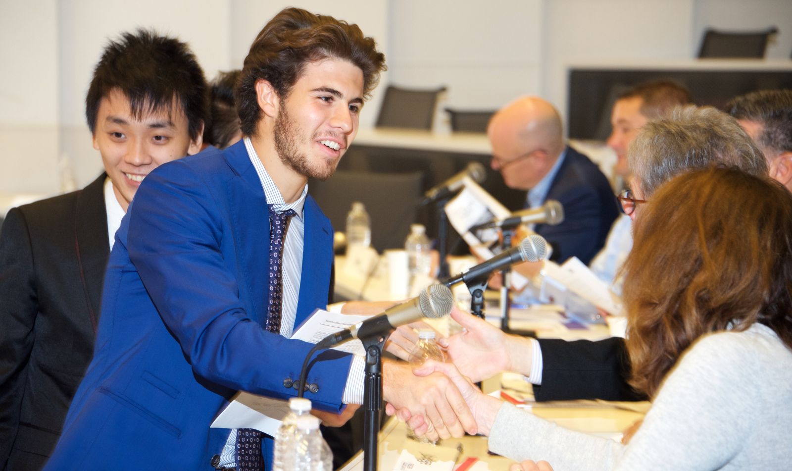 Male student smiling while shaking hands with a seated panel judge