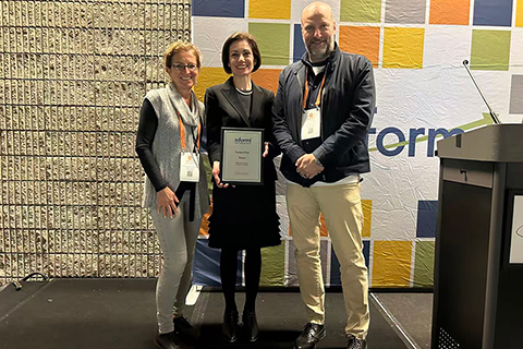 UW ECE Maryam Fazel stands on a stage, holding an award certificate. The award presenters stand on either side of her.