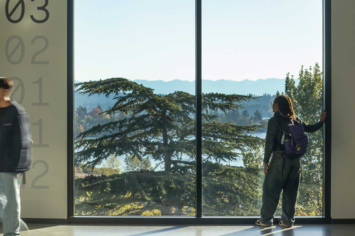 Student looking out of a large window at the trees and mountains visible from outside the IEB
