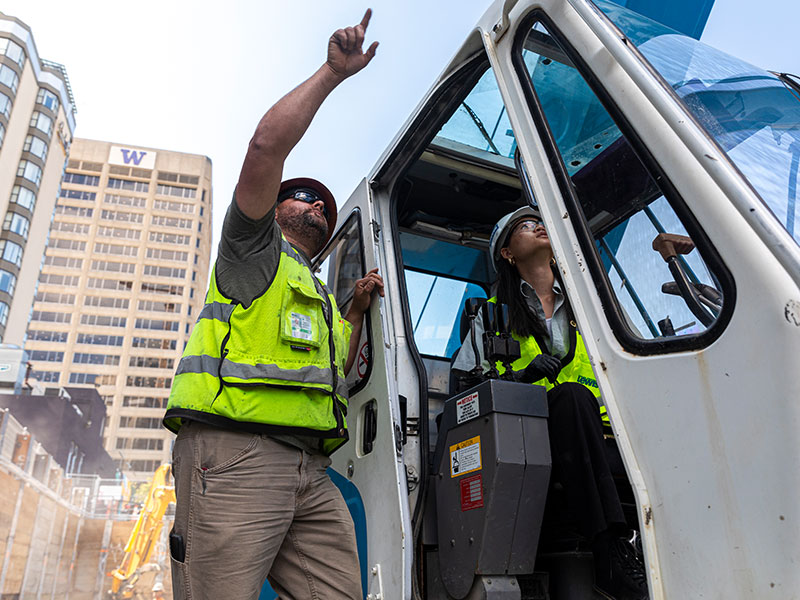 Individuals wearing high-vis vests and hard hats using heavy machinery in construction site