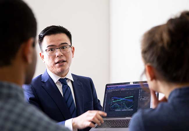 Professor showing two students a laptop screen, which shows a data visualization