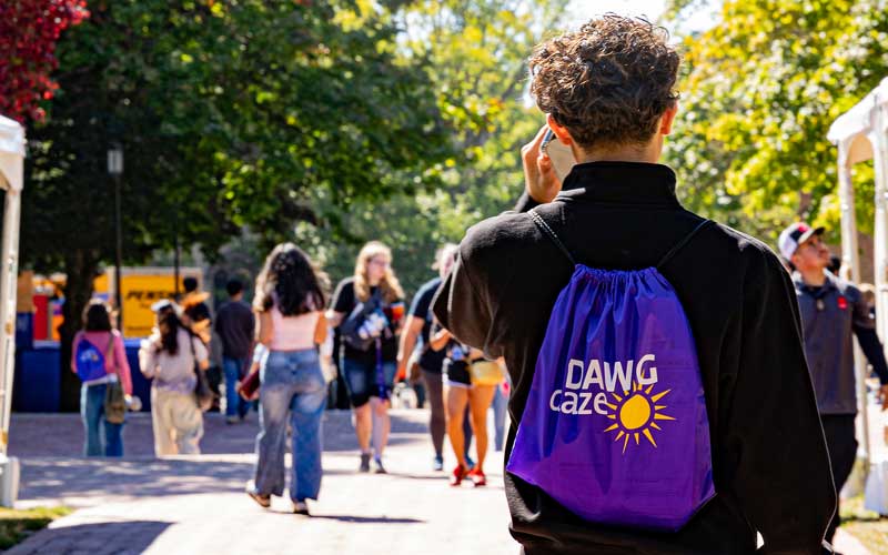 Student wearing "Dawg Daze" backpack walking on campus during the rush of move-in day