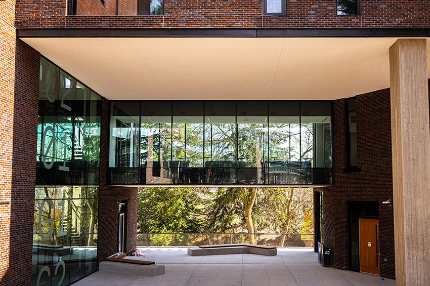 Modern building with a suspended glass passageway between two brick structures and a courtyard below.