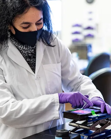 Person in lab coat and gloves monitoring prototype using smartphone
