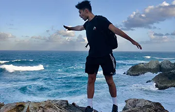 young man standing on a rock with water behind him