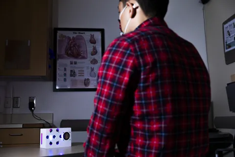 A small white box on a table and a person sitting in front of it (their back is to the camera)
