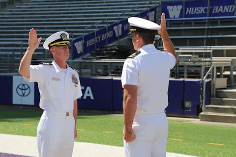 Two military officers in white uniform with their right arm raised at Alaska Airlines Field at Husky Stadium