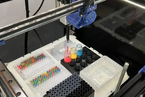 Jubilee drops pink liquid into a small glass, surrounded by several other small containers filled with different colors