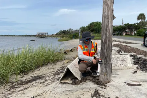 A person on a beach checking a wave gauge attached to a pole