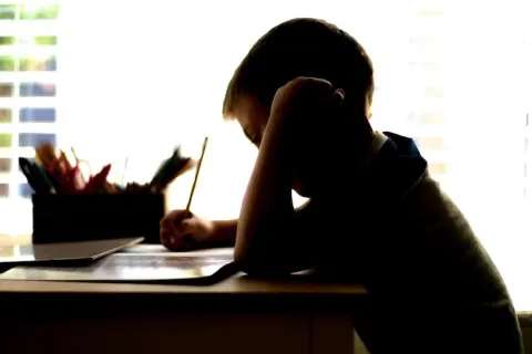 Young person sitting at a desk writing with a pencil