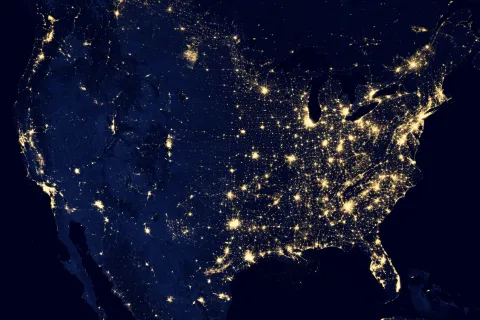 Satellite image of the United States at night, showing concentrated clusters of city lights