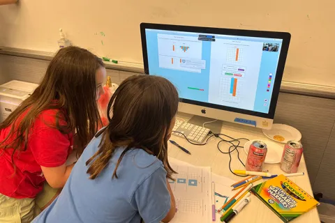 Two children play a game on a computer.