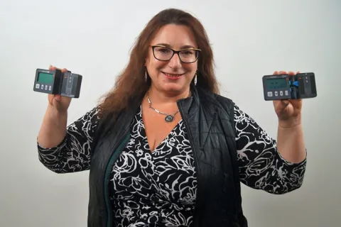 Beth Kolko holds the drip assist device while smiling for the camera
