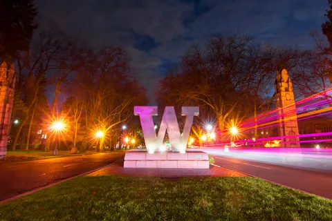 A bronze W statue at the entrance to the University of Washington campus at night