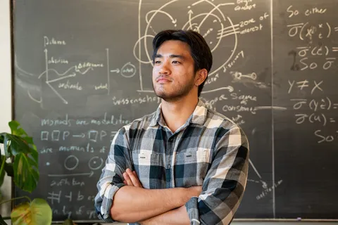 Photo of Andre Ye in front of a chalkboard with philosophy-related information on it.