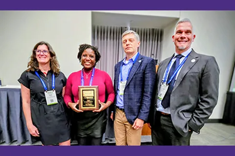 Four people smile for the camera while standing with a rectangular award plaque.