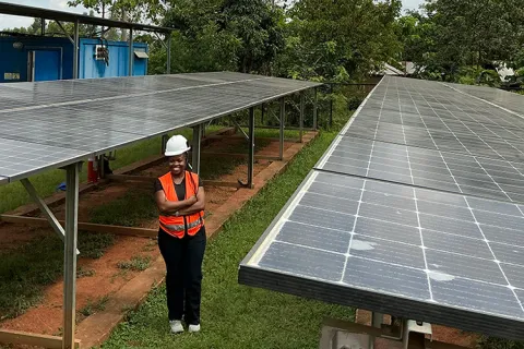 Eliane Nirere wearing a hardhat and standing between two solar panels outdoors
