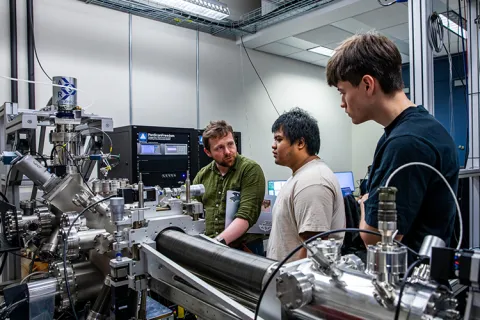 Three people stand next to a complex metal tube-shaped machine