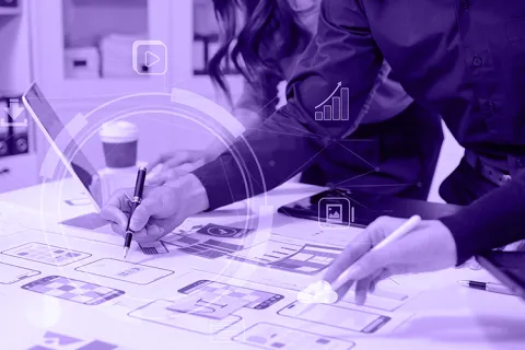 Two people reviewing wireframes and interface sketches spread across a table.