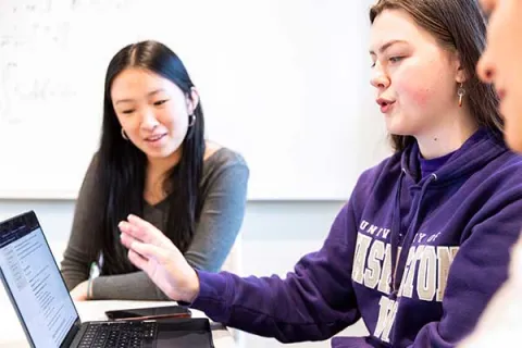 Students huddled together over laptop reviewing document