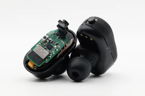 Two black earbuds: one with the casing removed exposing a computer chip and tiny camera.