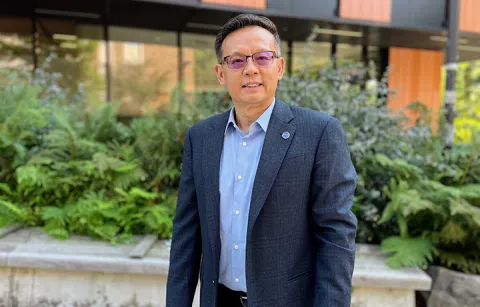 Juming Tang standing outdoors in front of a research building on campus.