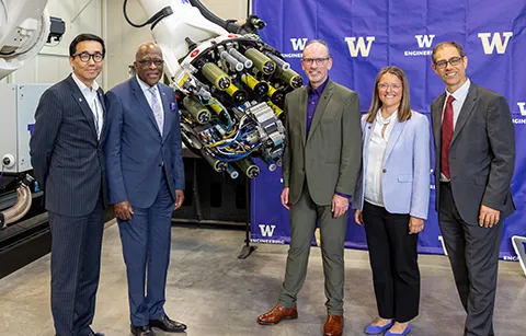 Group photo taken during UW event. Group is in front of large, advanced machinery