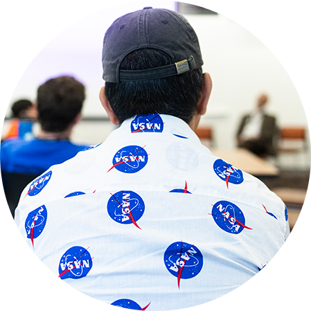 a student wearing a shirt with NASA logo all over it sitting with his back to the camera.
