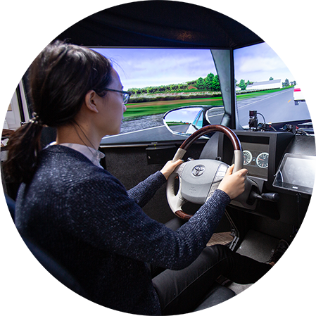 A researcher holding  a steering wheel facing a road way simulation