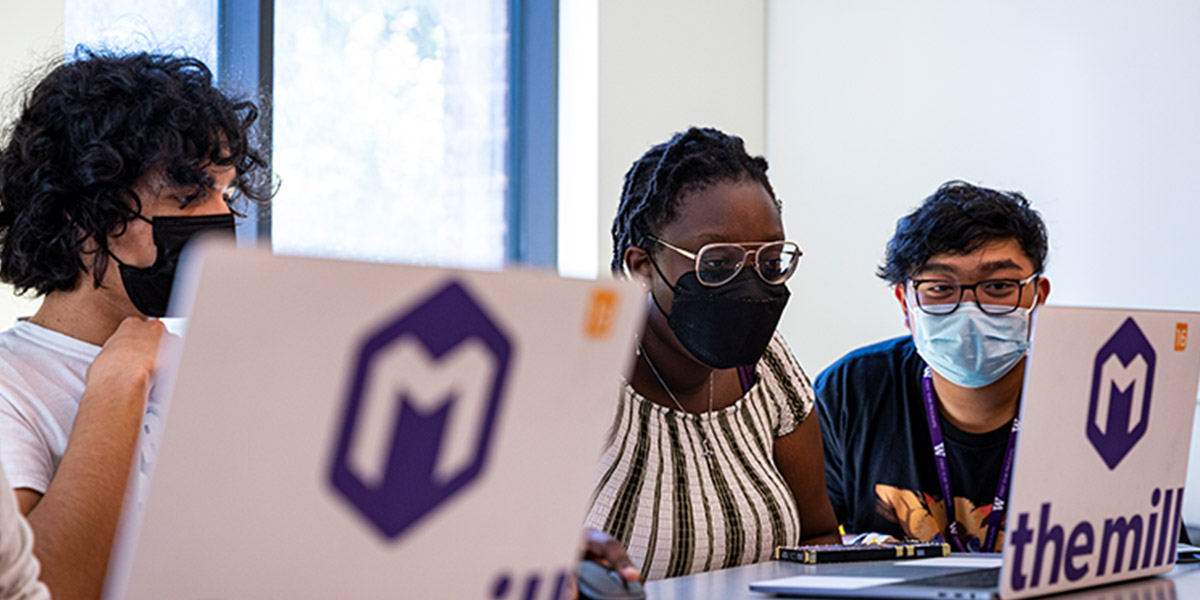 Three masked students looking into one laptop screen