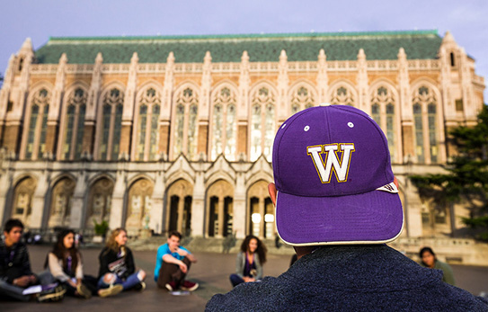 a student wearing a purple UW cap facing a group of students sitting in Red Square