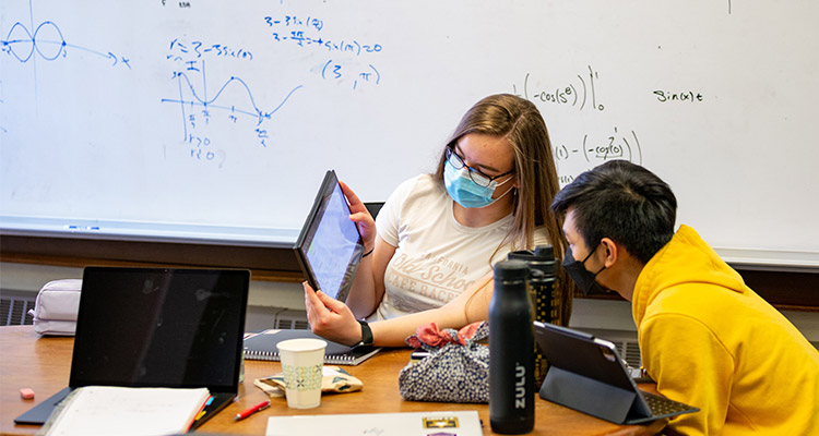 Two students working together on homework using an iPad and whiteboards