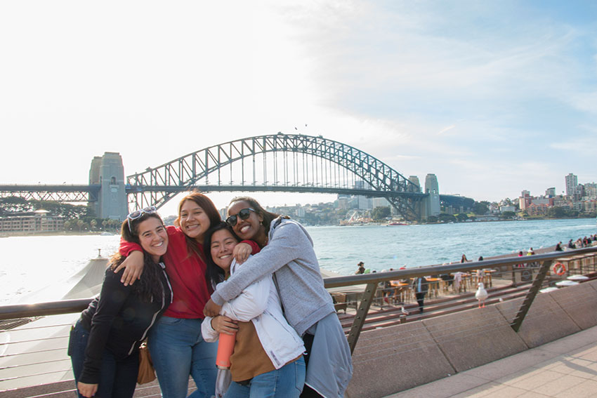 Four students hugging in front of the Sydney Harbour Bridge