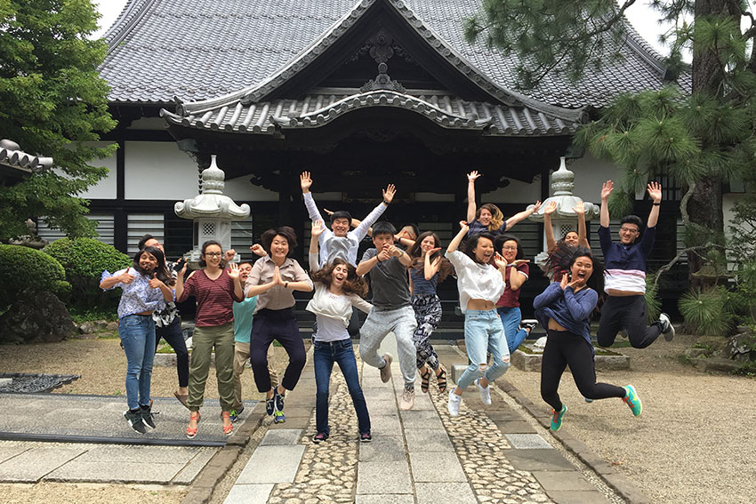 A group of students jumping in the air in front of a traditional Japanese building