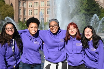 A group of students smiling by a campus fountain